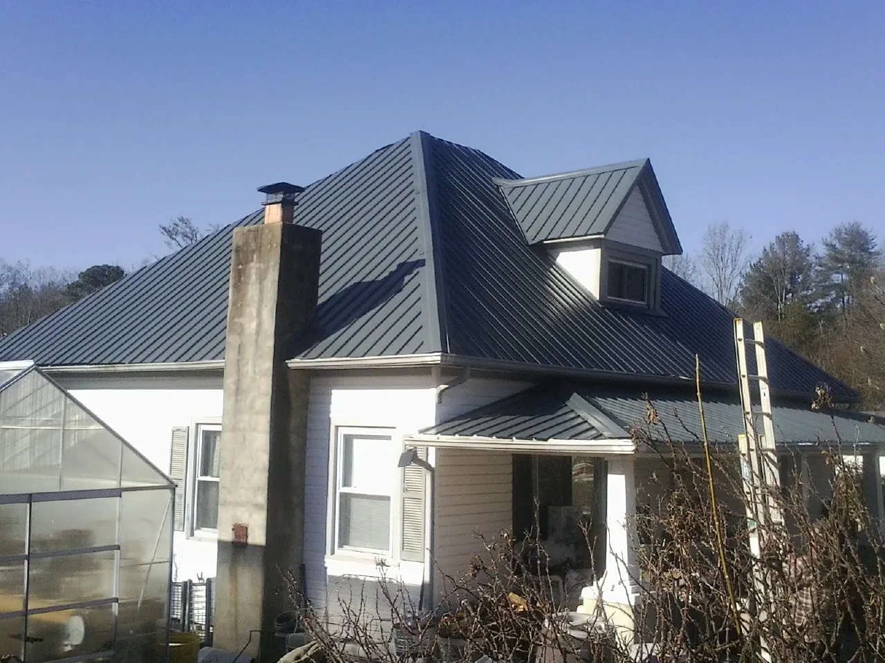 Dark blue standing seam metal roof on a white farmhouse with dormer — Slate & Tile Roof Repair by Roofing Brothers in Ashland